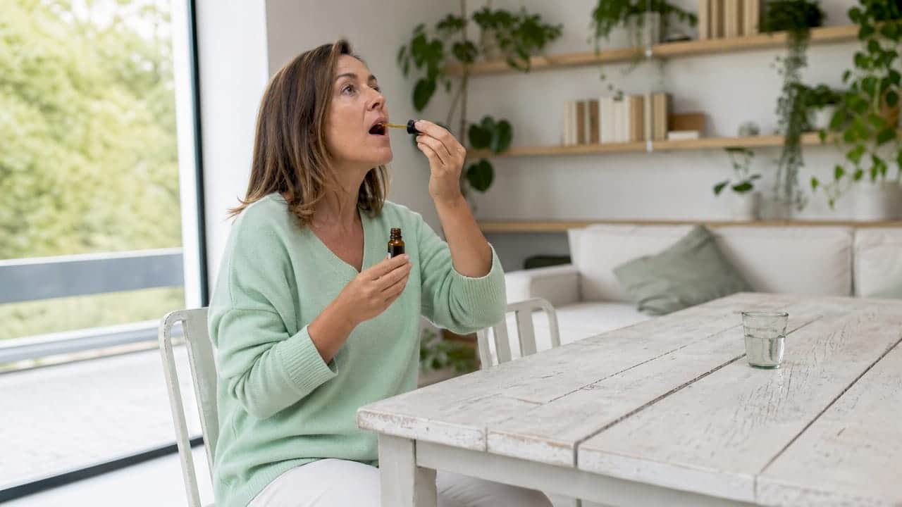 A woman uses a dropper to take CBD oil at home.